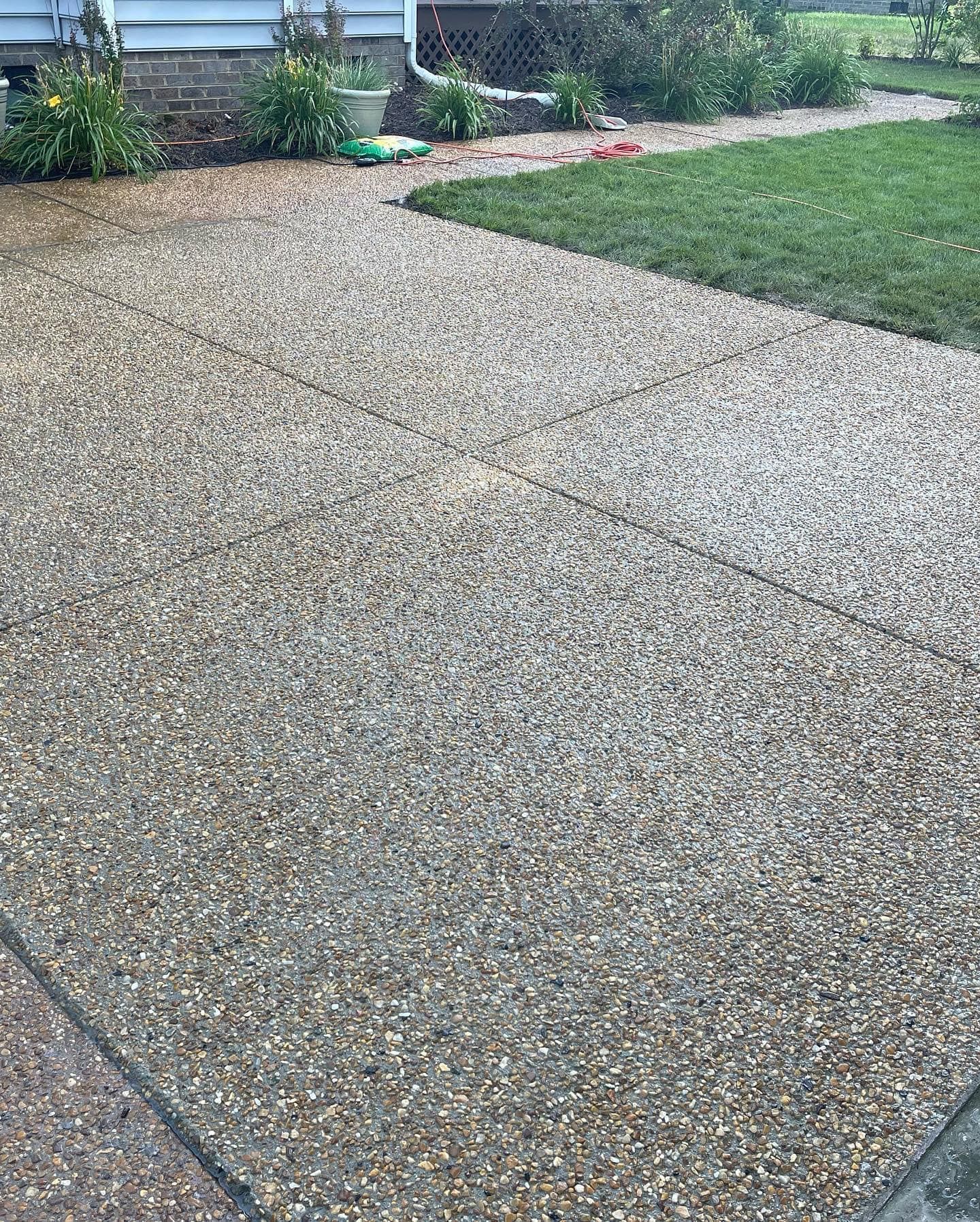 Exposed aggregate concrete pathway. Wet from rain, leading toward green lawn and garden.