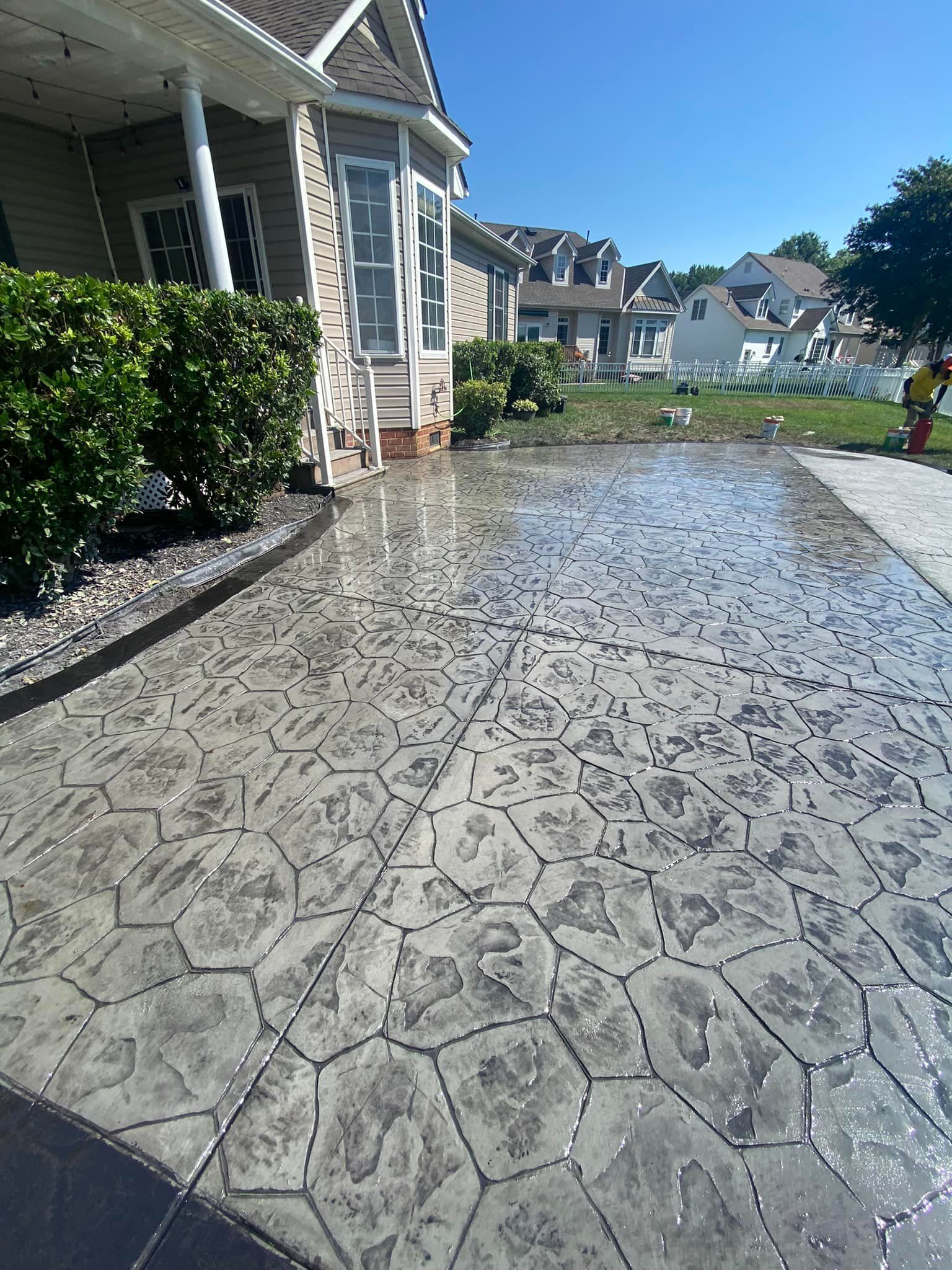 Wet, patterned concrete driveway in front of a house on a sunny day.