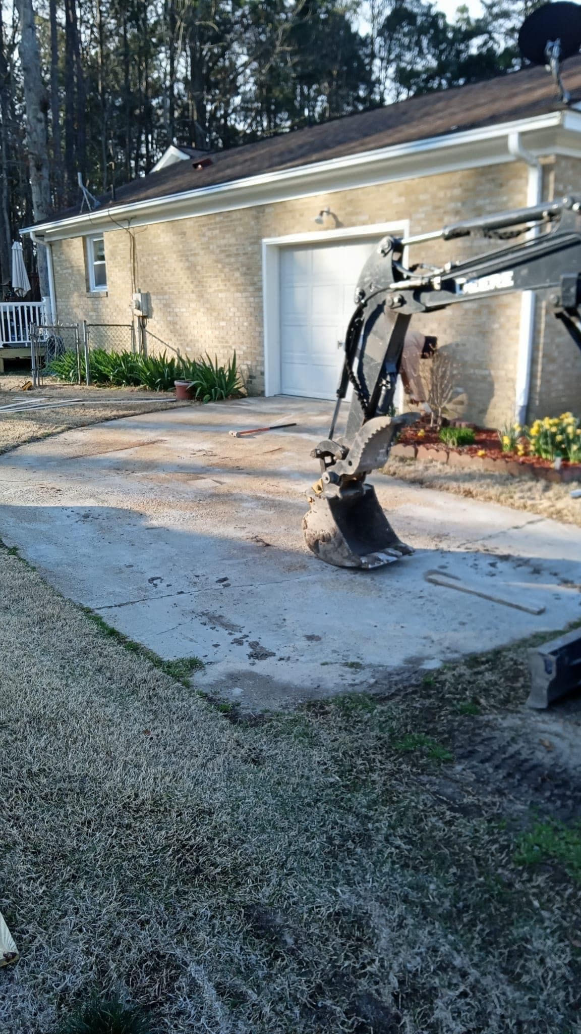 An excavator working on a concrete pad in front of a beige building with a white garage door.