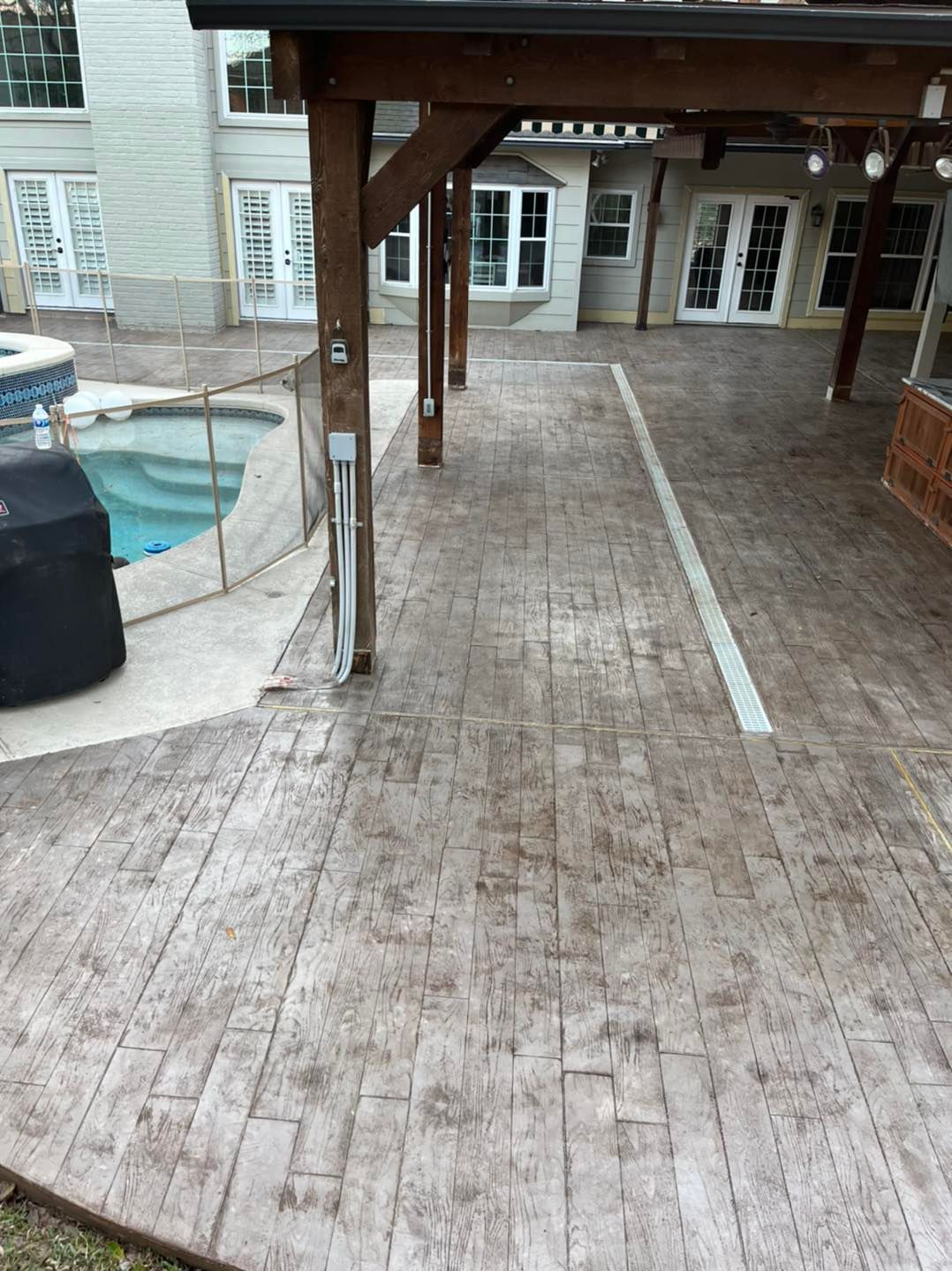 Patio with stamped concrete, a pool, and wooden pergola.
