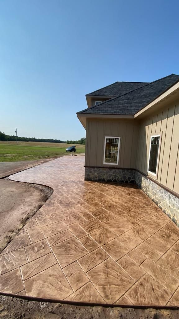 Stamped concrete patio next to a tan house with a blue sky in the background.