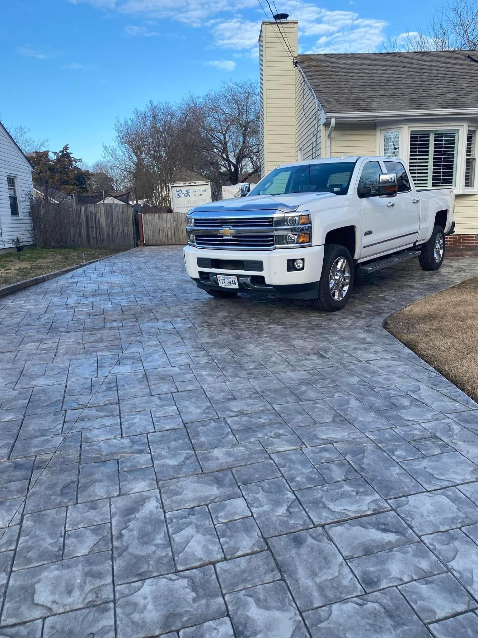 White pickup truck parked on a stone paver driveway in front of a house on a sunny day.