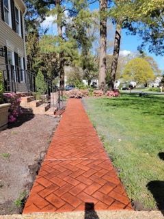 Red brick pathway leading from a house with a porch to a grassy yard on a sunny day.