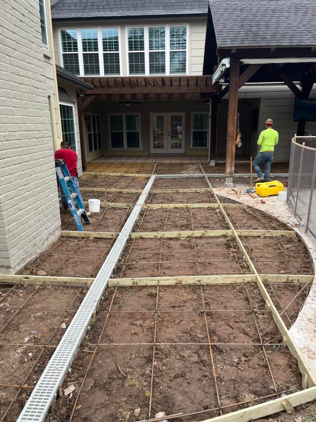Construction workers building an outdoor patio with wooden frames and a drainage system near a house.