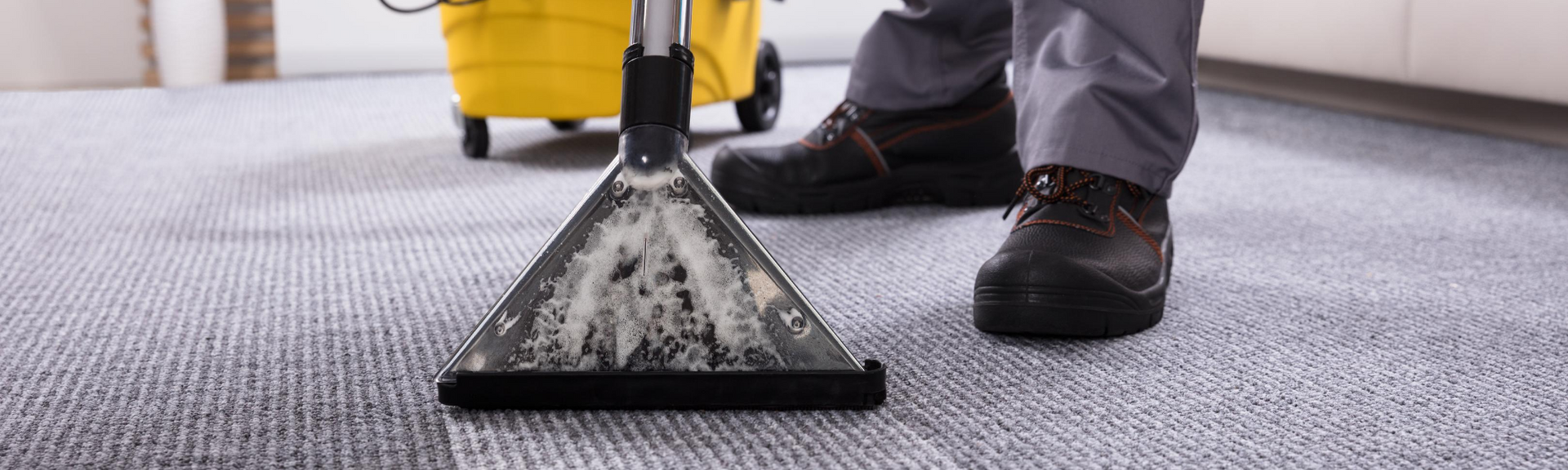 Worker vacuuming carpet beside a yellow cleaning machine in a hallway