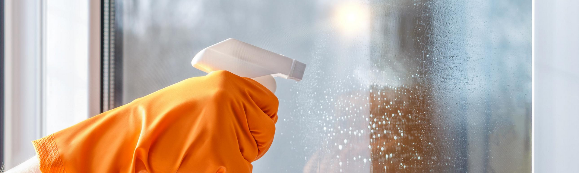 Orange-gloved hand cleaning a fogged window with a white squeegee