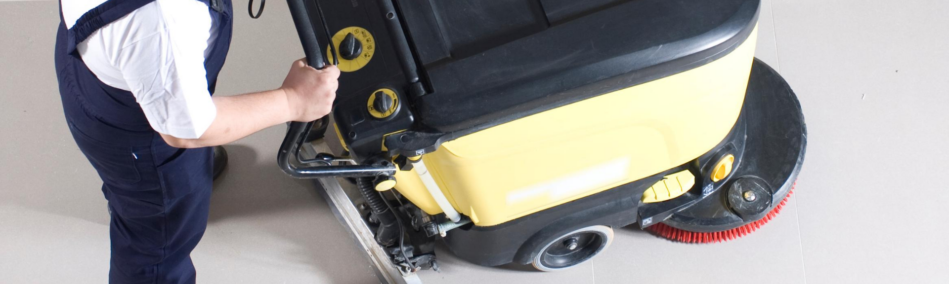 Person cleaning a yellow floor scrubber, close-up of machine controls and front brush