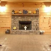 Wood-paneled room with a stone fireplace, autumn decor, and a wooden floor