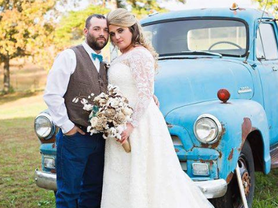 Bride and groom posing beside a vintage blue truck outdoors with autumn foliage