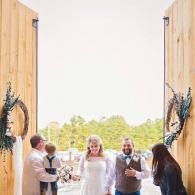 Wedding party walking through open barn doors outdoors at a bright ceremony entrance