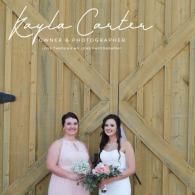 Two people in dresses holding a bouquet in front of a wooden barn door