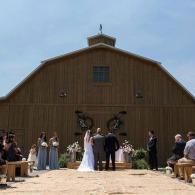 Wedding ceremony outside a large wooden barn under a blue sky