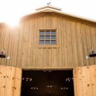 Wooden barn facade with open double doors and a small window above, sunlit from the left.