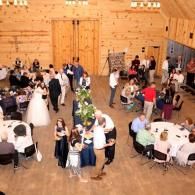 People mingling at round tables in a rustic wood-paneled wedding reception hall