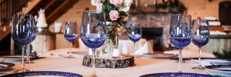 Elegant dining table with blue wine glasses, white plates, candles, and a floral centerpiece.