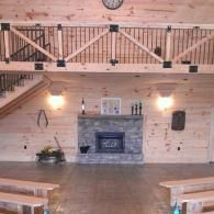 Rustic hall with wood floors, stone fireplace, hanging light, and wooden railing above benches
