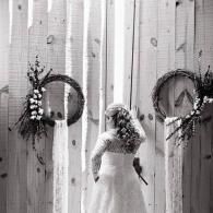 Bride in a white gown standing before rustic wooden doors with floral wreaths