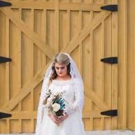 Bride in a white dress and veil holding a bouquet in front of a wooden barn door