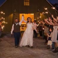 Newlyweds walking through a sparkler send-off outside a barn at dusk