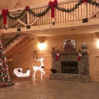 Holiday-decorated cabin interior with lit Christmas tree, glowing reindeer, and garlanded balcony staircase