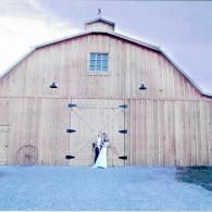 Bride and groom standing at the large barn doors of a weathered wooden barn