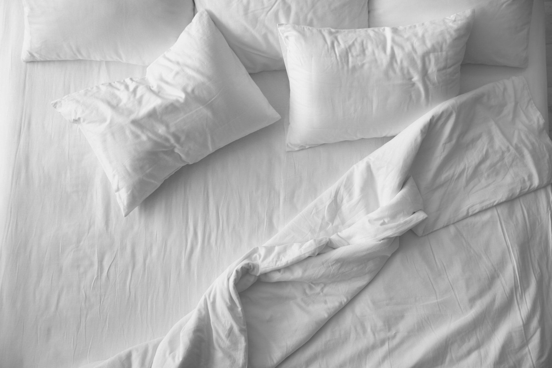 Vue de dessus d'un lit bien fait avec des oreillers blancs et une couette blanche partiellement pliée.