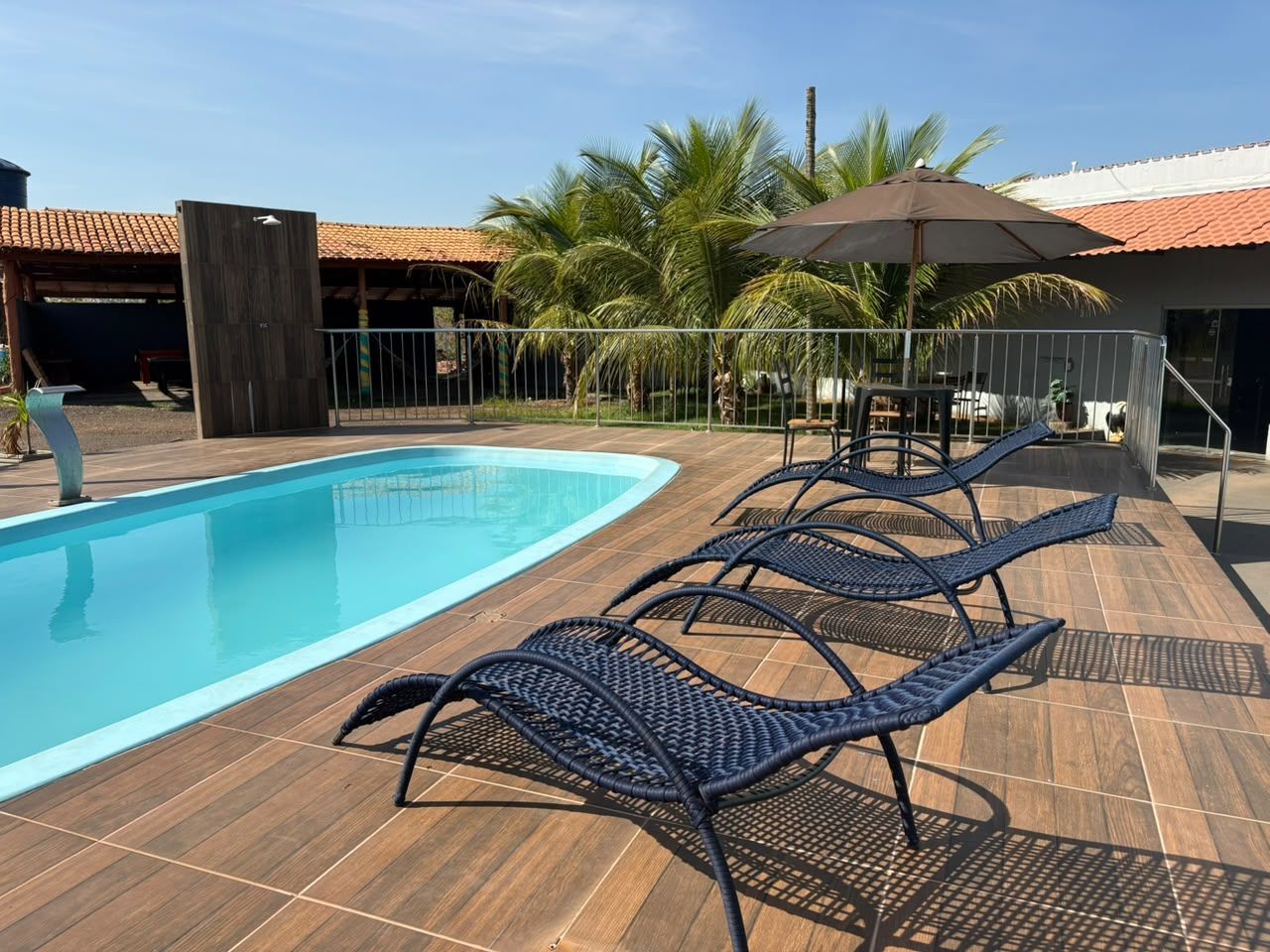 Espreguiçadeiras à beira da piscina em um deck de madeira ao lado de uma piscina turquesa e palmeiras.