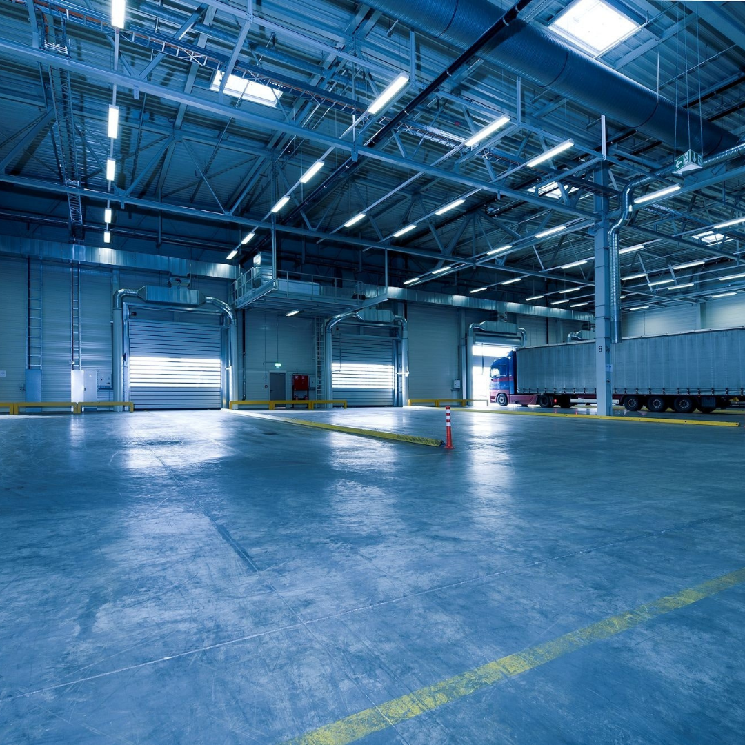 Large, blue-toned warehouse interior with loading docks and a semi-truck parked at one bay.