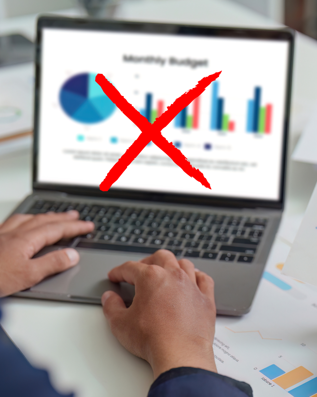 A person working on a laptop with a budget chart on the screen, crossed out with a large red X.