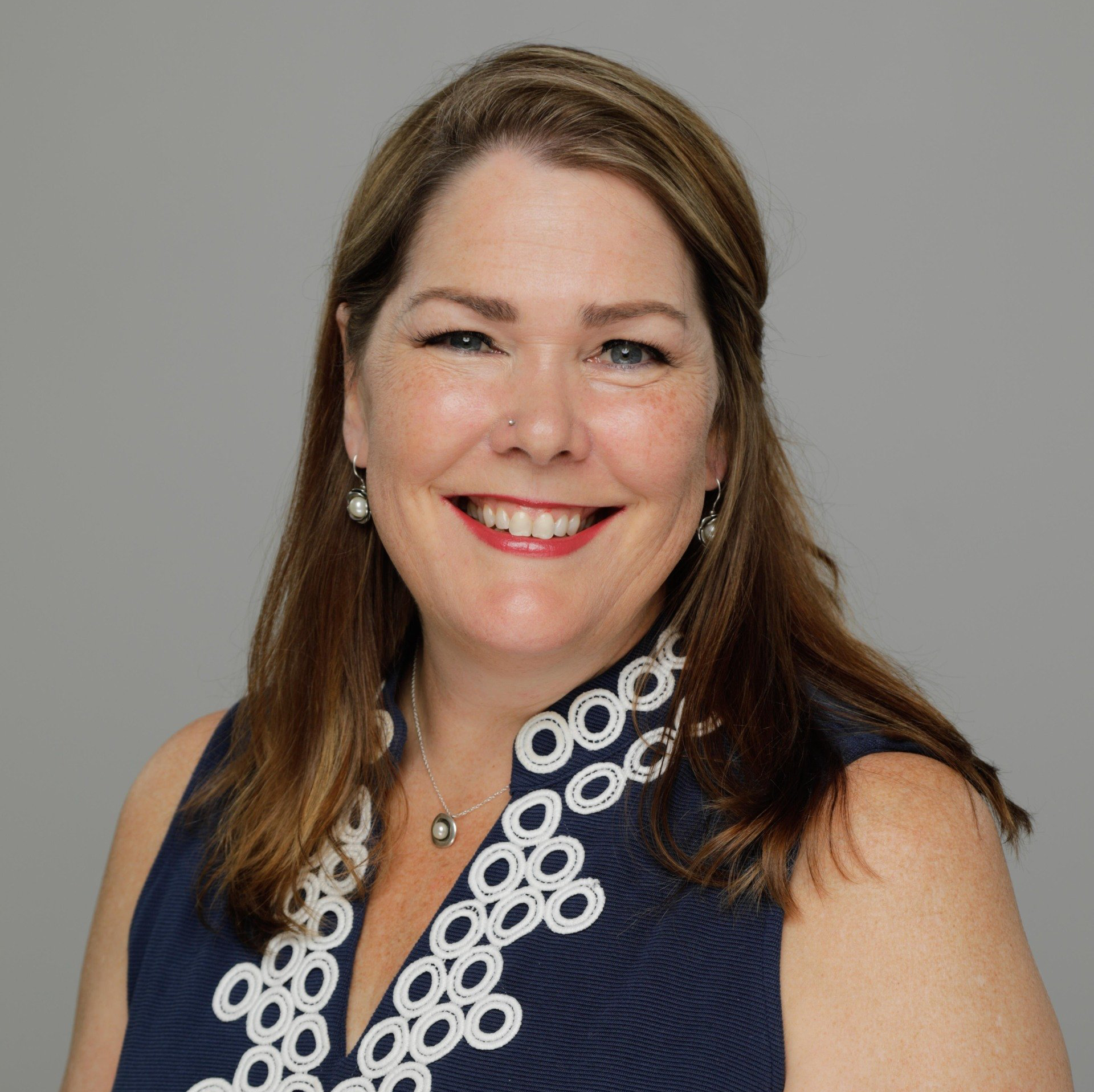 A woman wearing a blue top and a necklace is smiling for the camera.