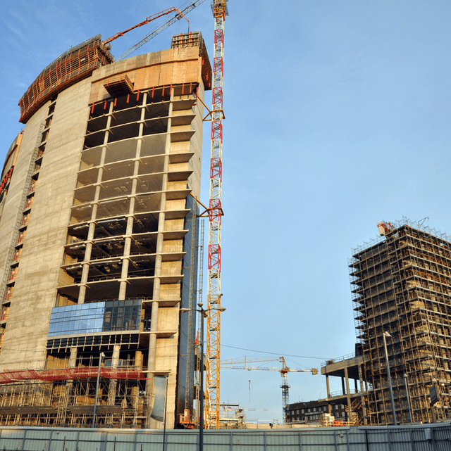 Construction site with tall buildings and cranes under a blue sky.