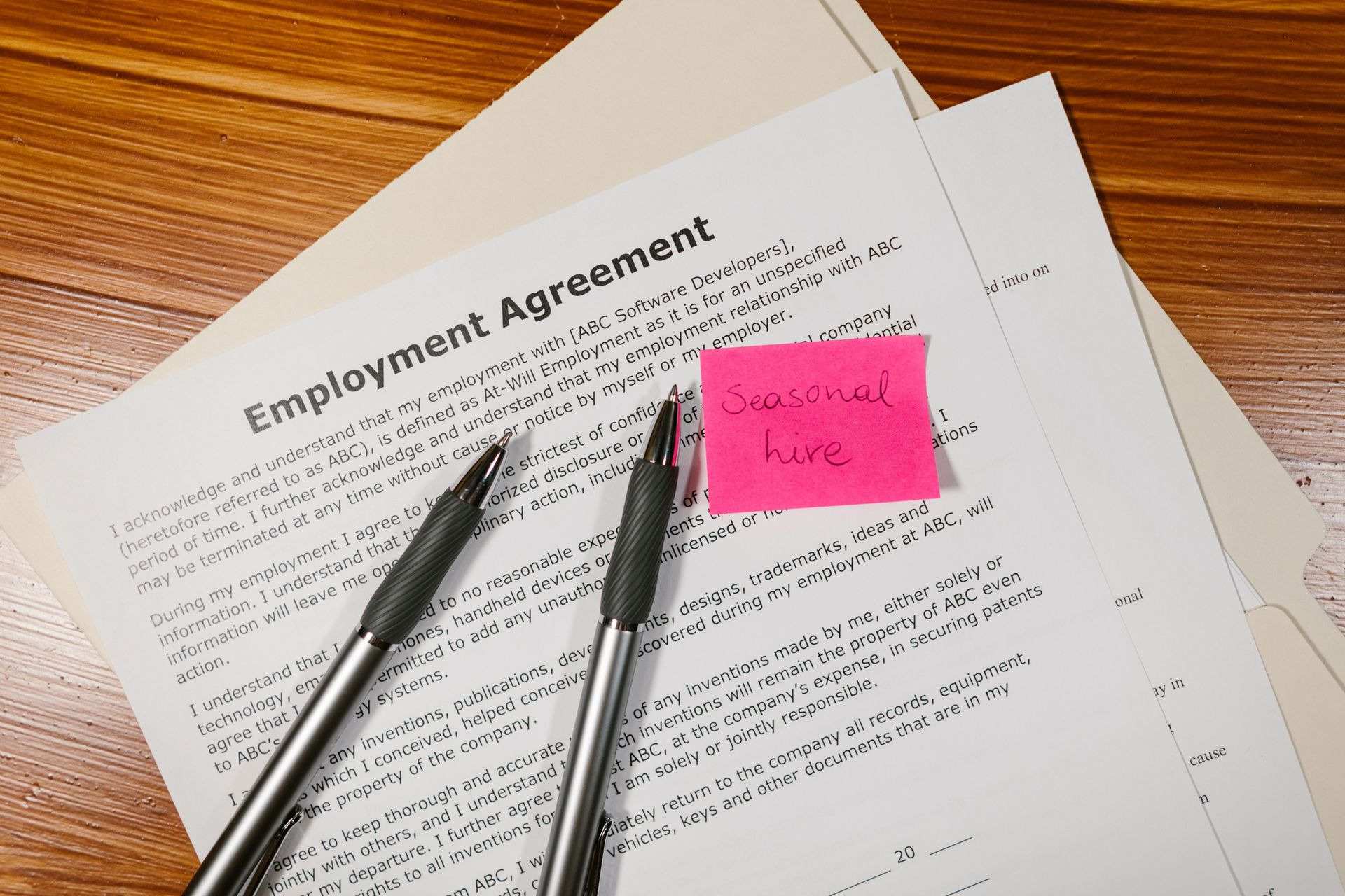Employment agreement with two pens and a pink sticky note on a wooden desk