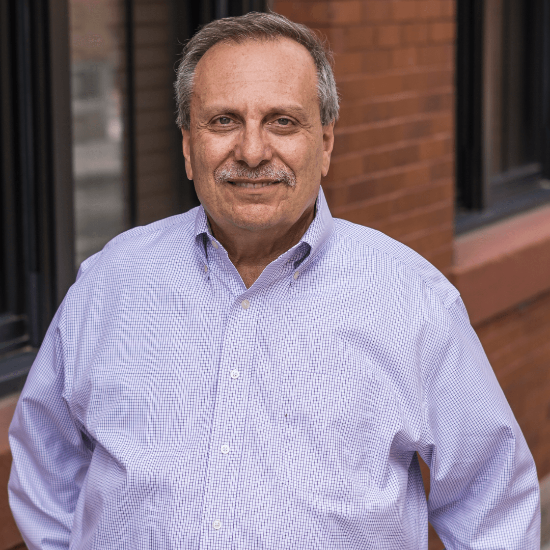 A man in a plaid shirt is standing in front of a brick building.