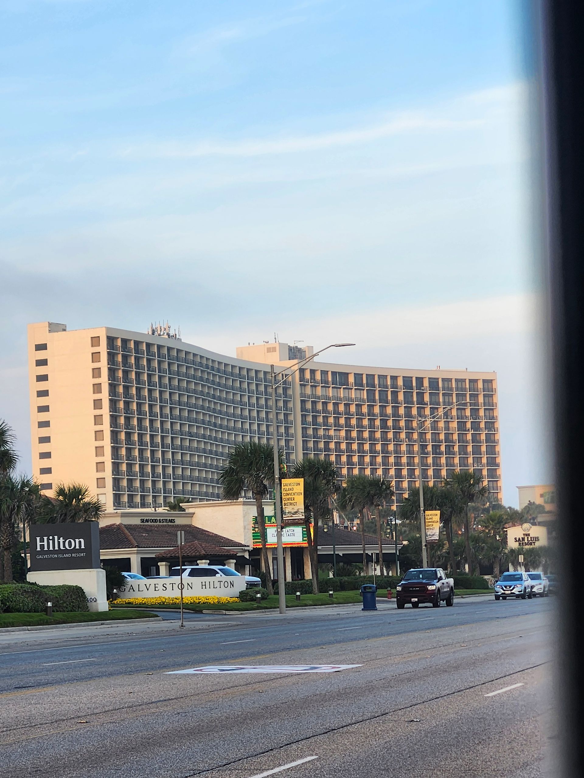 Hilton hotel beside a busy road at dusk, with cars and a blue sky in the background