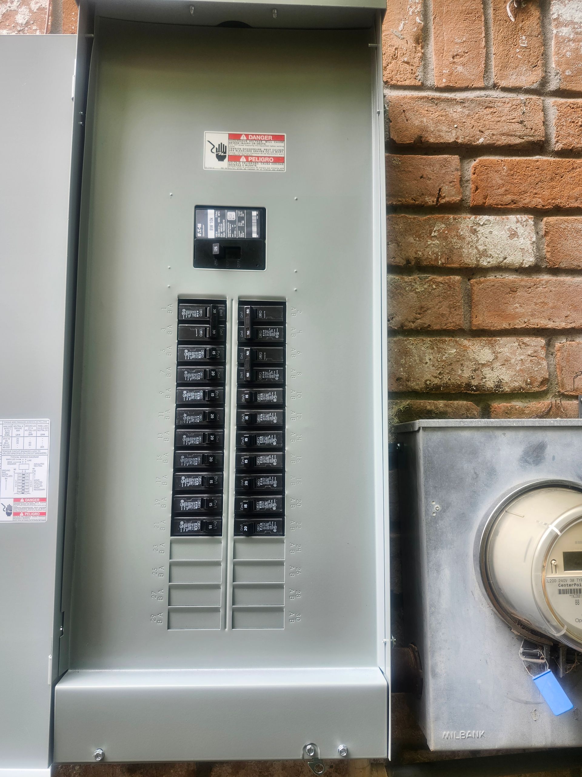 Open electrical breaker panel with switches beside a brick wall and gas meter.