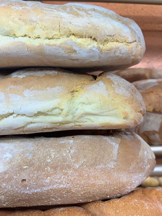 Pagnotte di pane rustico impilate su uno scaffale di una panetteria, con la crosta spolverata di farina.