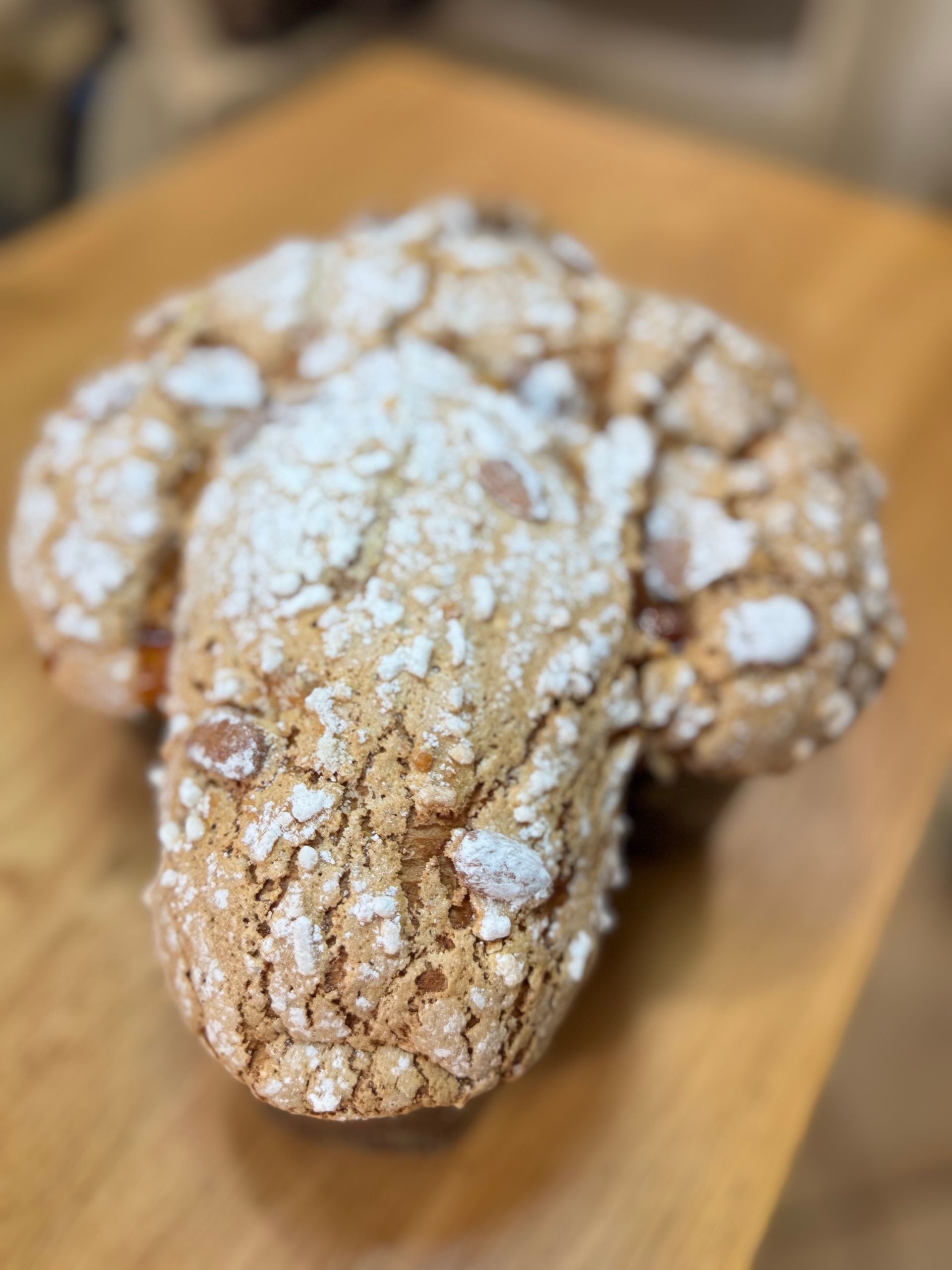 Tre biscotti increspati ricoperti di zucchero a velo su un tagliere di legno, uno davanti e due dietro.