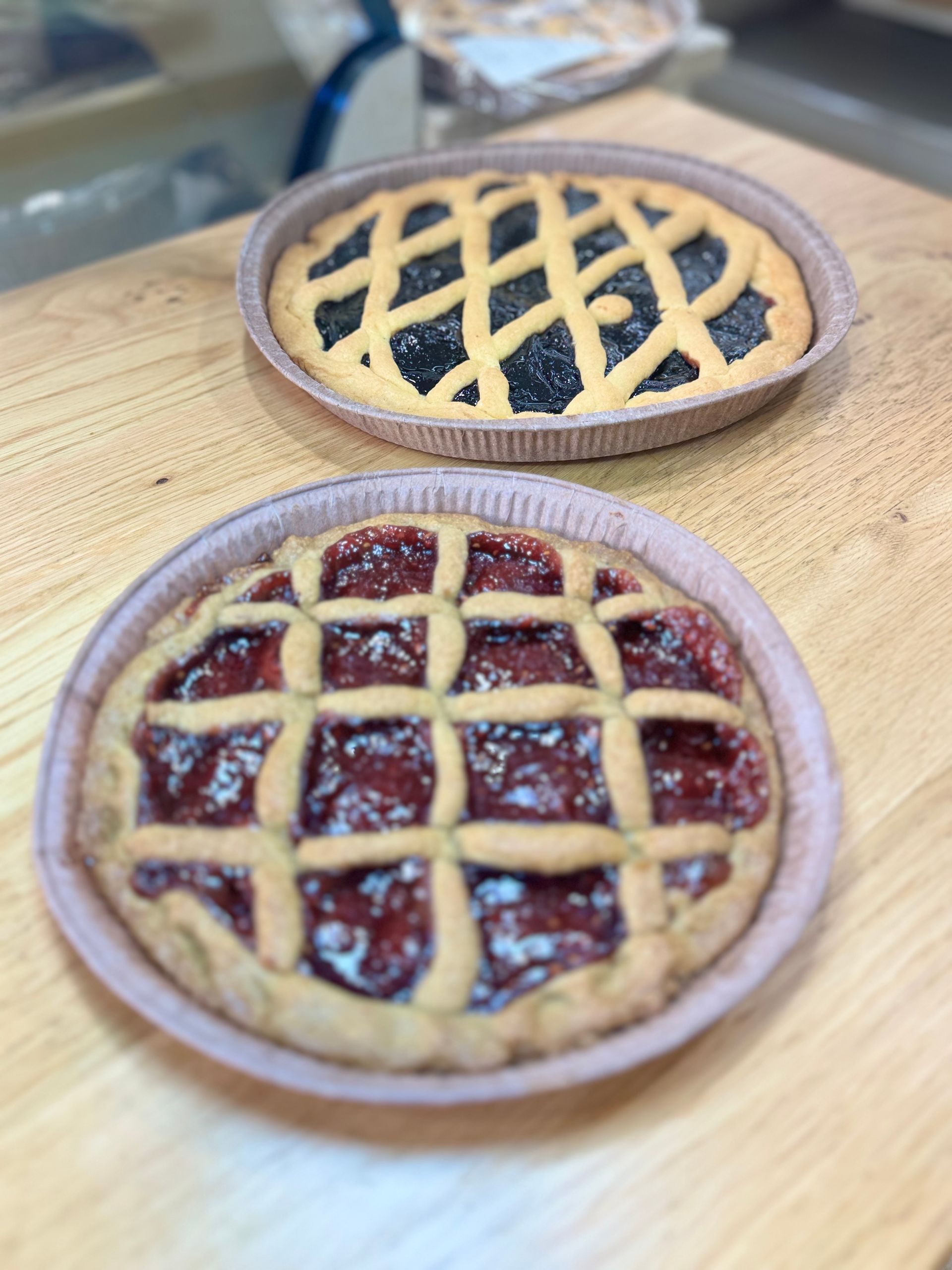 Due torte con copertura a grata su un bancone di legno, una con ripieno di frutti di bosco scuri e l'altra con ripieno di frutta più chiara.