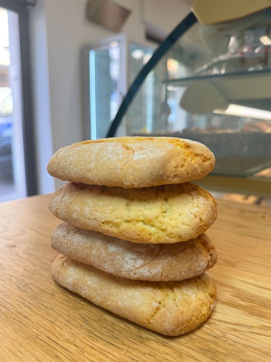 Pila di quattro biscotti ricoperti di zucchero a velo su un tavolo di legno in un ambiente interno.