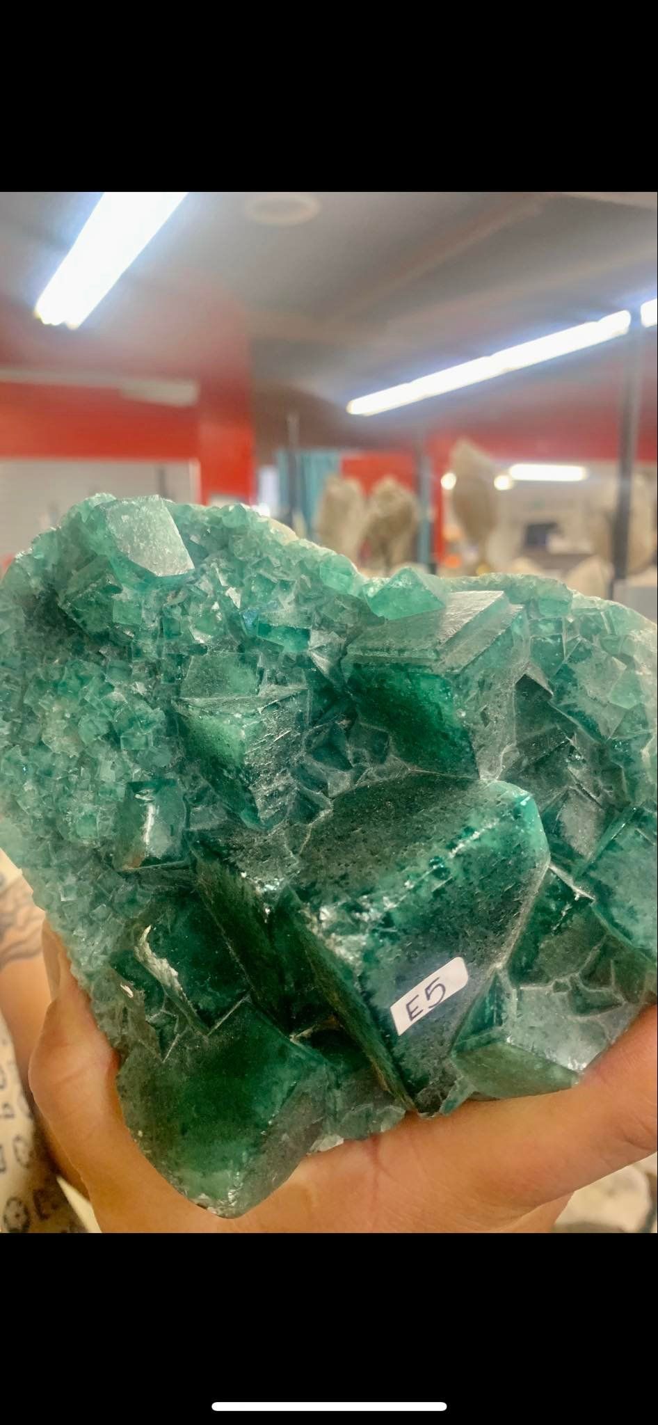 A person holds a large, green crystal formation. The setting is a store with orange accents.