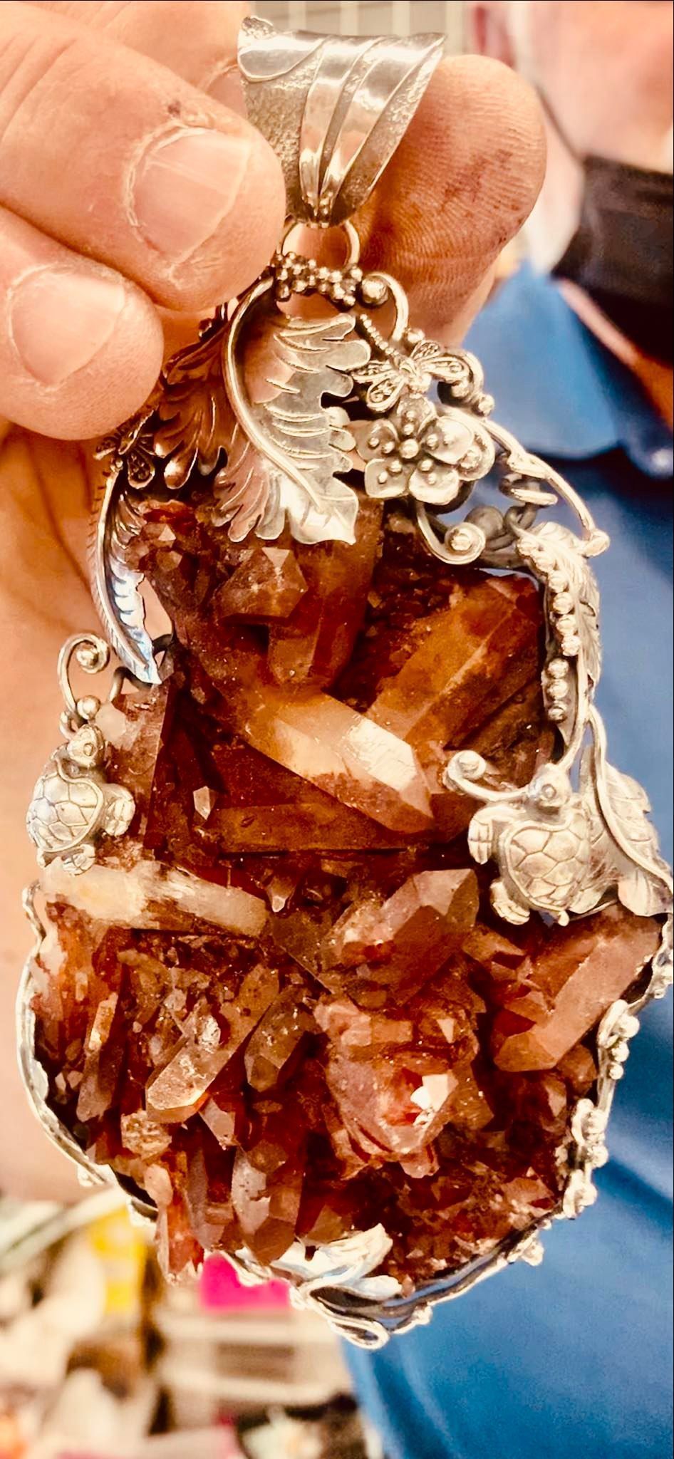 A person holding a large pendant with a silver frame and brown crystal cluster.