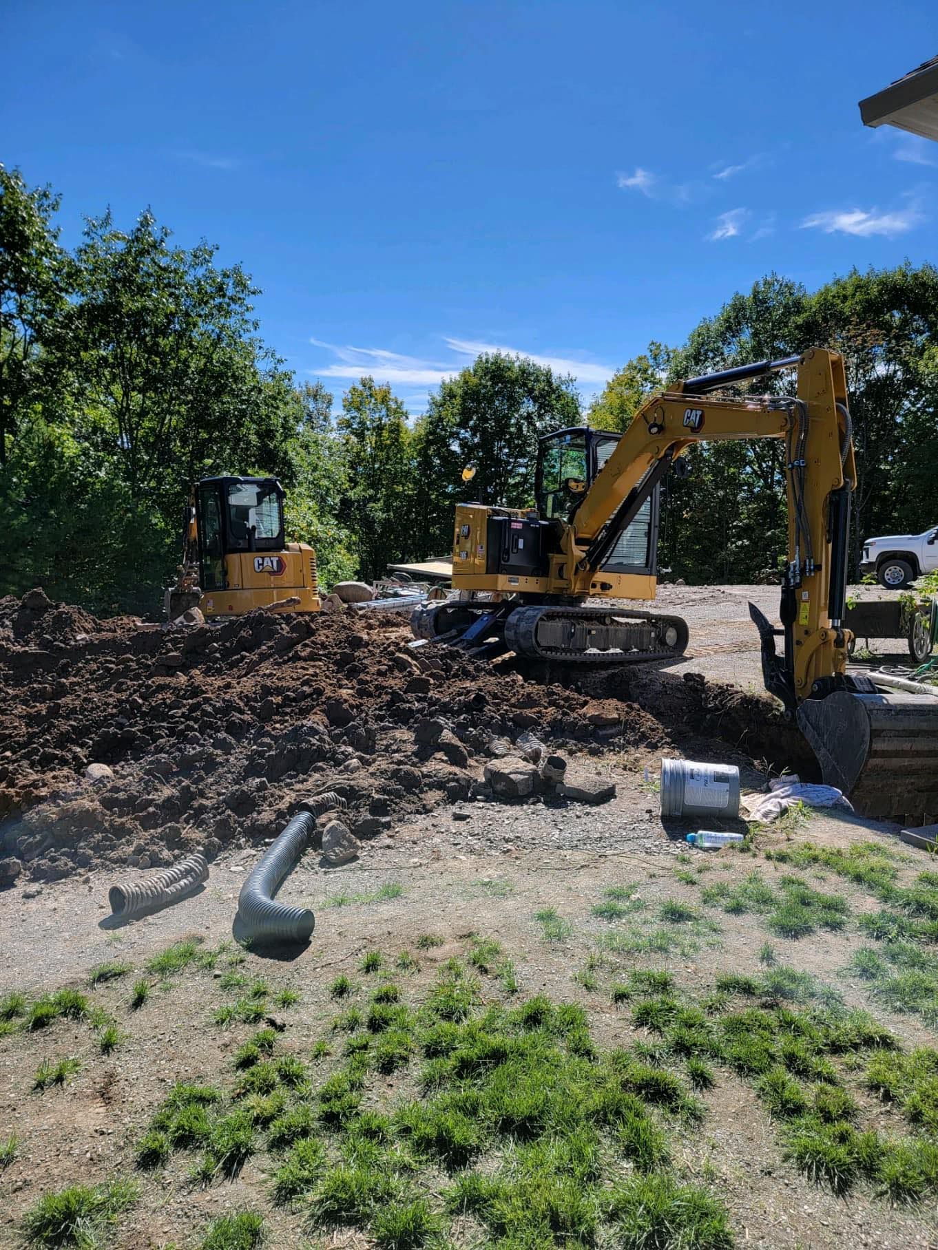 Two yellow CAT excavators on a construction site digging dirt under a blue sky.