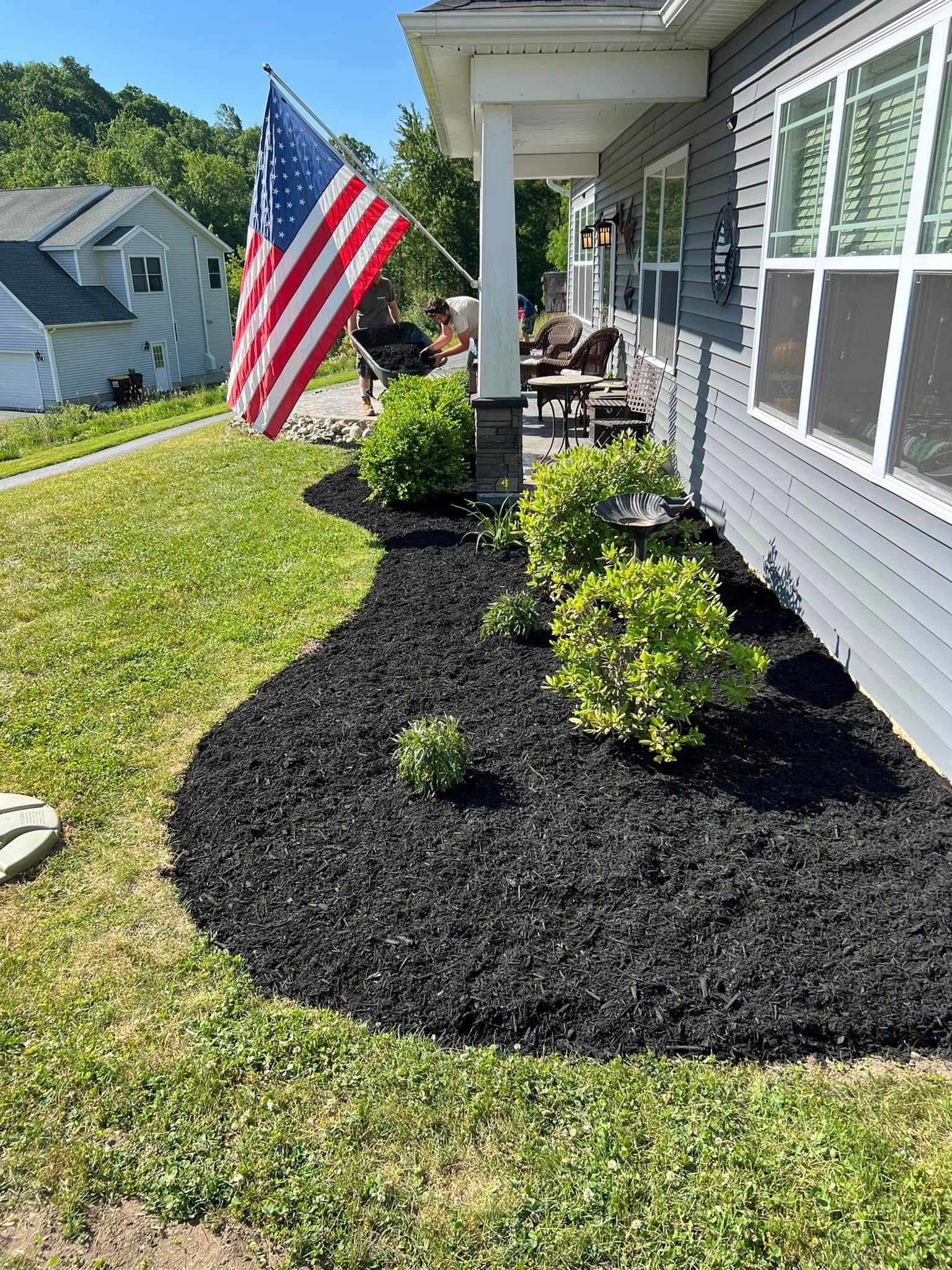 A house with a black mulch flower bed and an American flag.