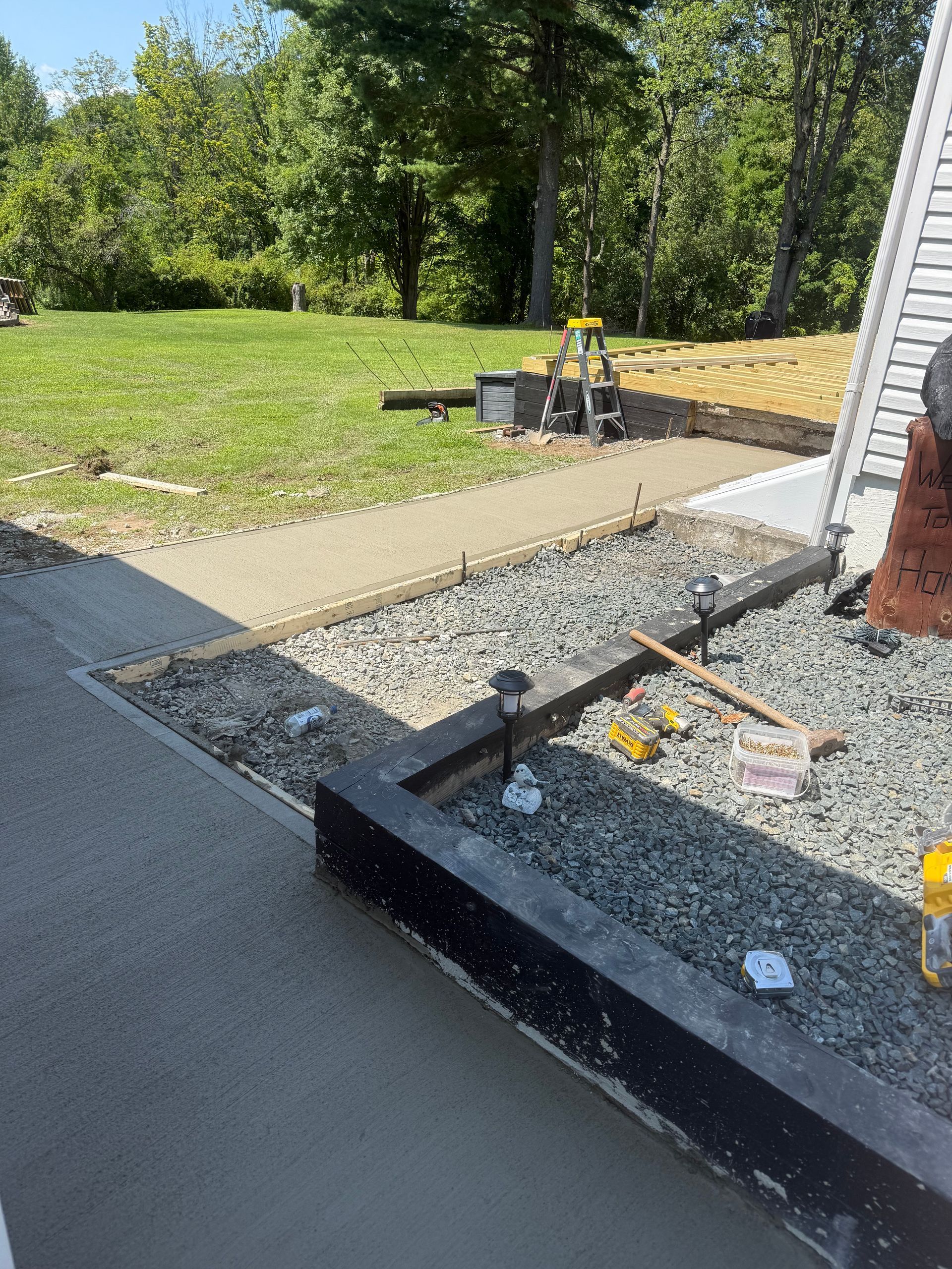 Newly poured concrete walkway and gravel landscaping next to a building, with a lawn in the background.