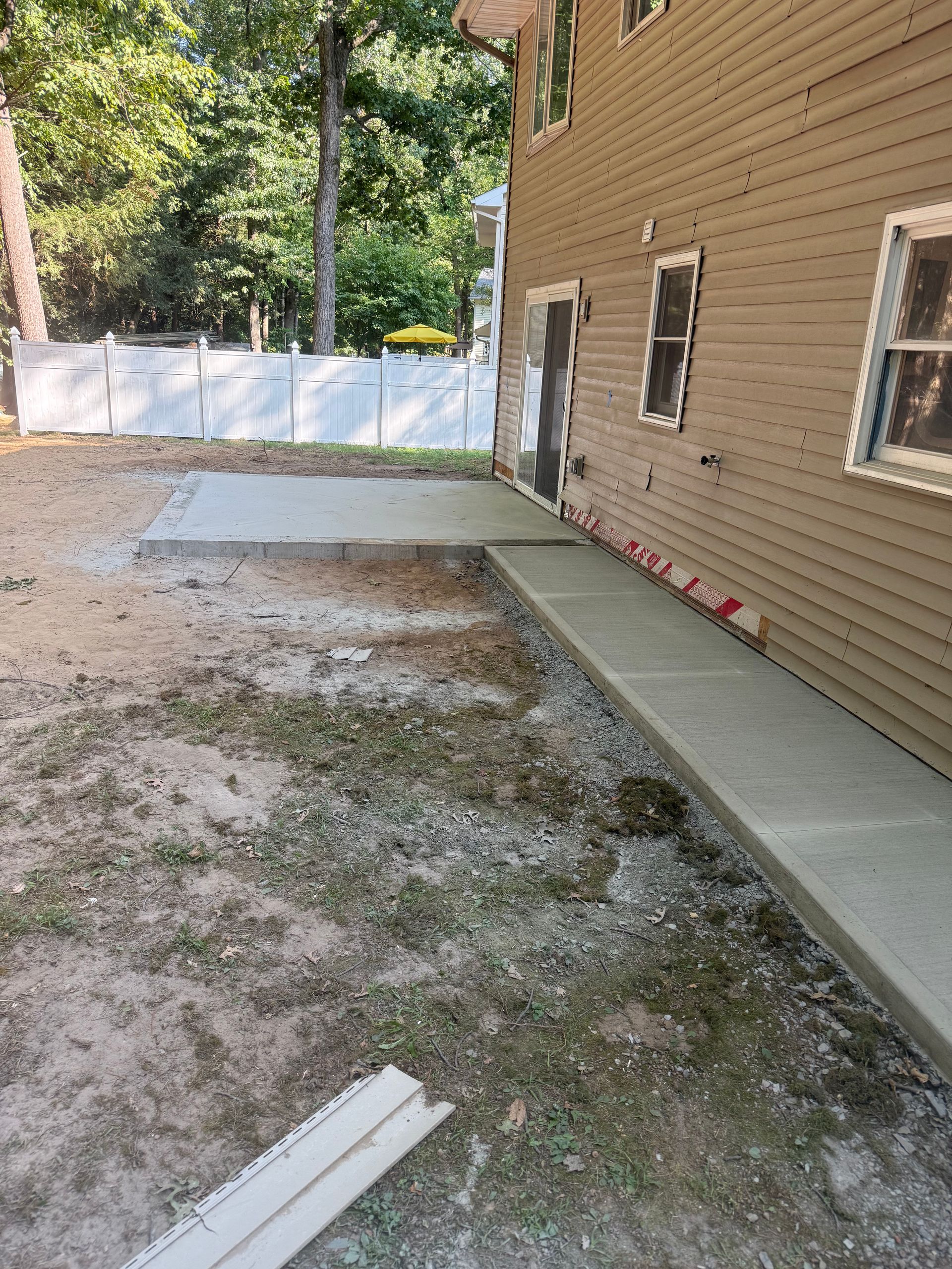 Newly poured concrete walkway and landing alongside a light brown building.