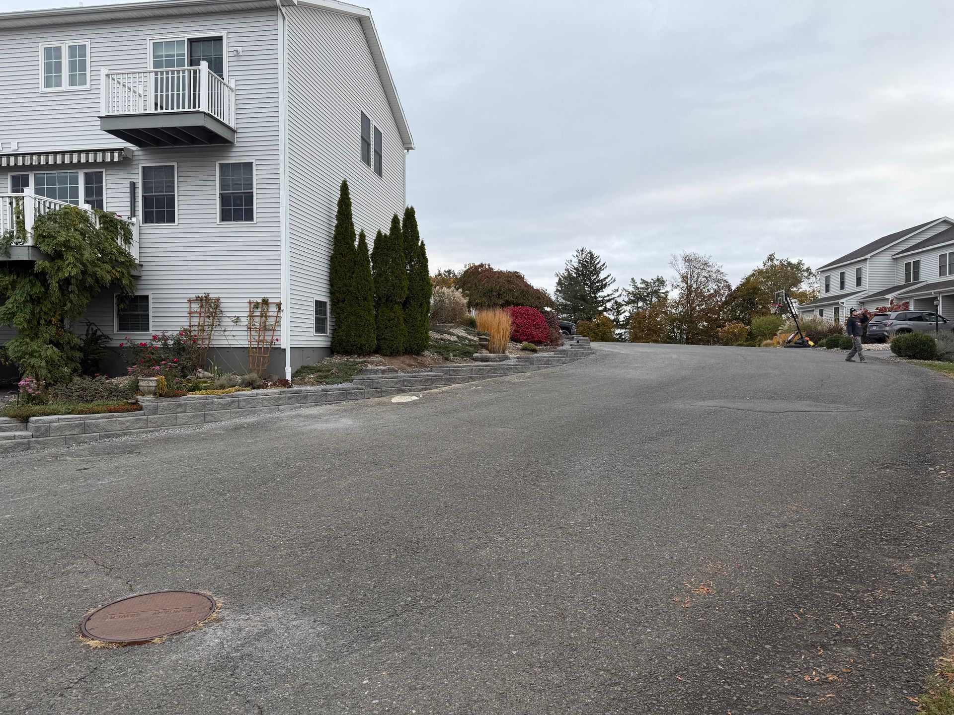 Gravel parking lot next to a two-story building with a balcony and landscaping. Overcast sky.