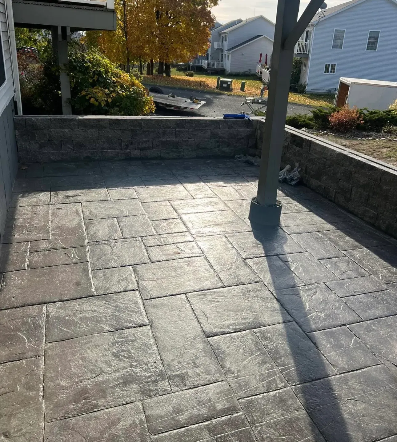 Stamped concrete patio with stone retaining wall. A wooden pillar casts a shadow.