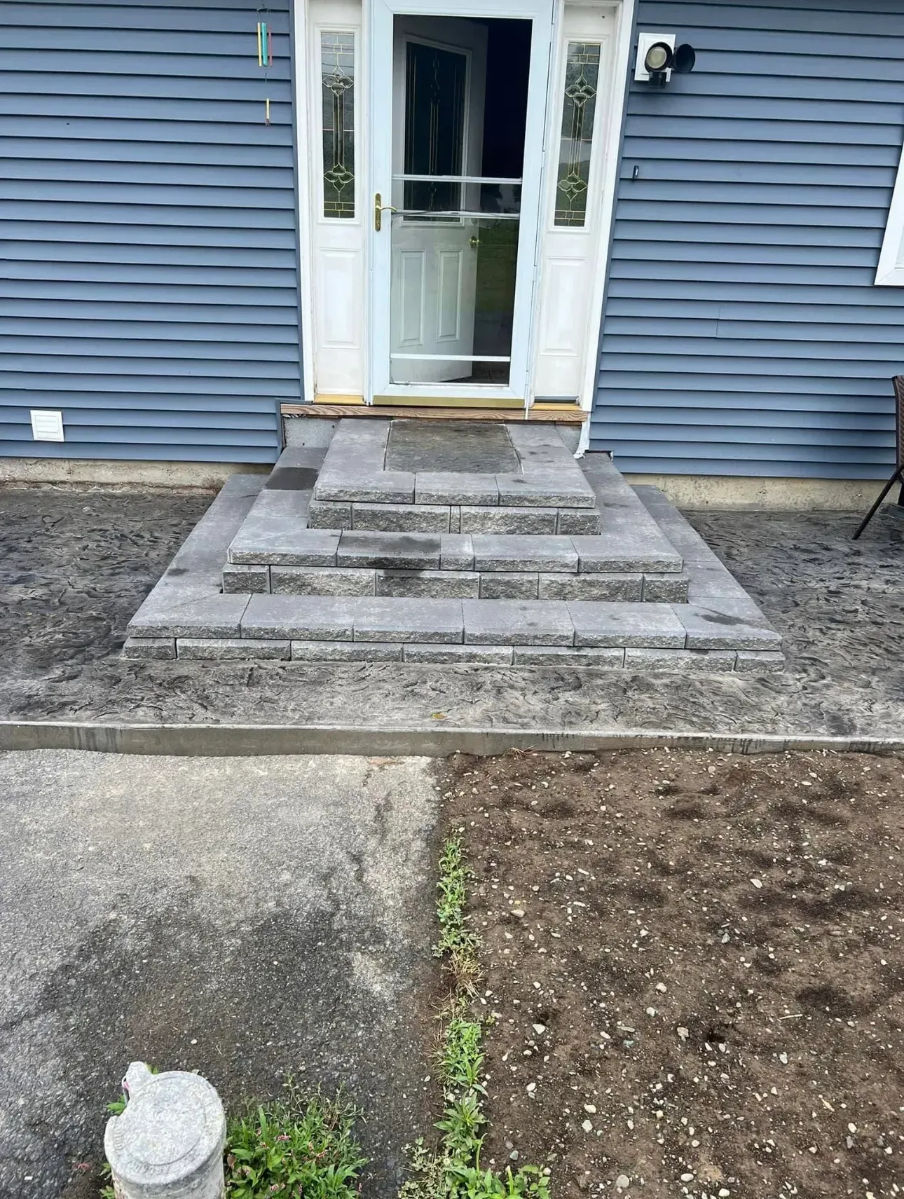 Gray stone steps leading to a white door with a screen door, set against a blue-sided house.