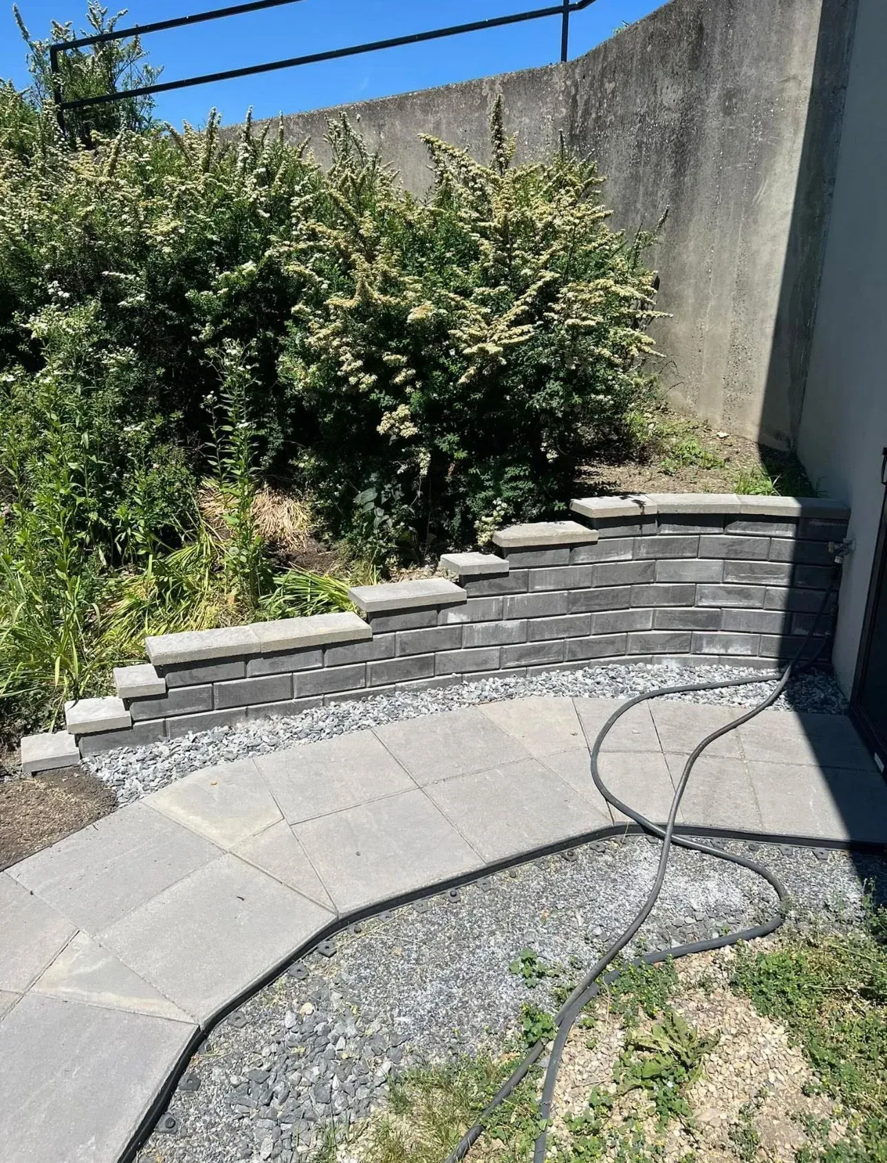 A stone retaining wall with steps, next to a paved pathway and greenery.