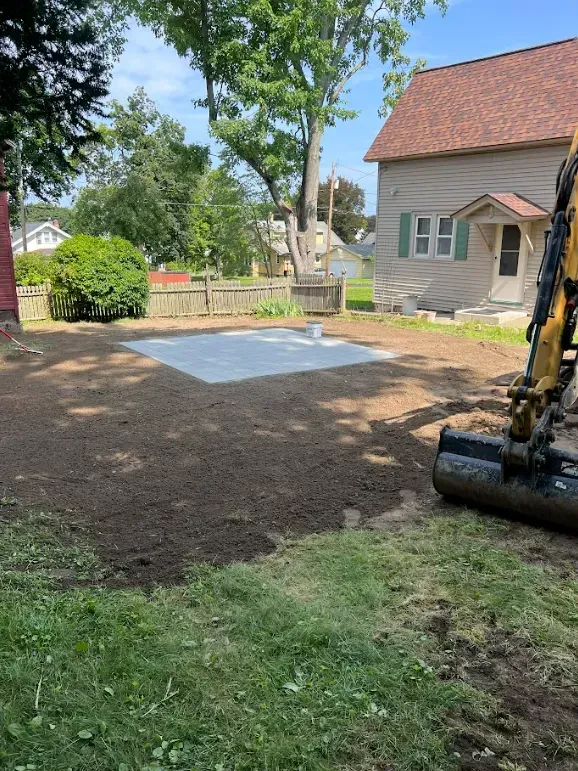 Backyard with dirt ground, a concrete pad, a house, and an excavator.